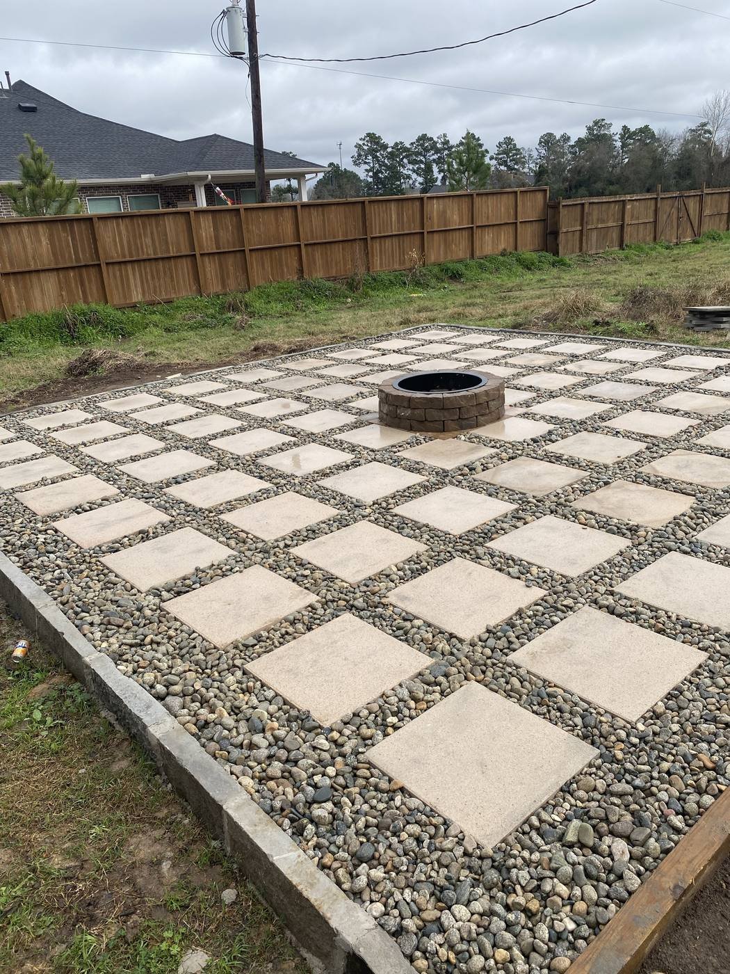 Grid-pattern paver patio with river rock infill and a stone fire pit