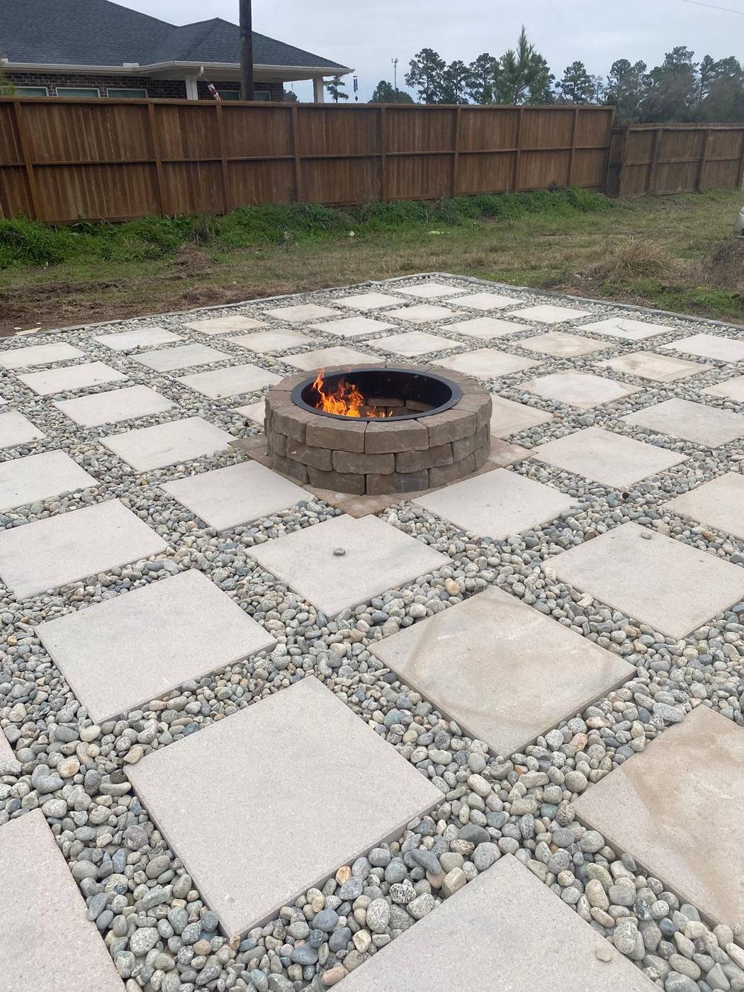 Grid-pattern paver patio with a stone fire pit, lit at dusk